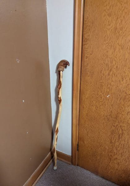 A wooden walking can with a craved eagle head resting against a wall | Photo by Diana Prairie