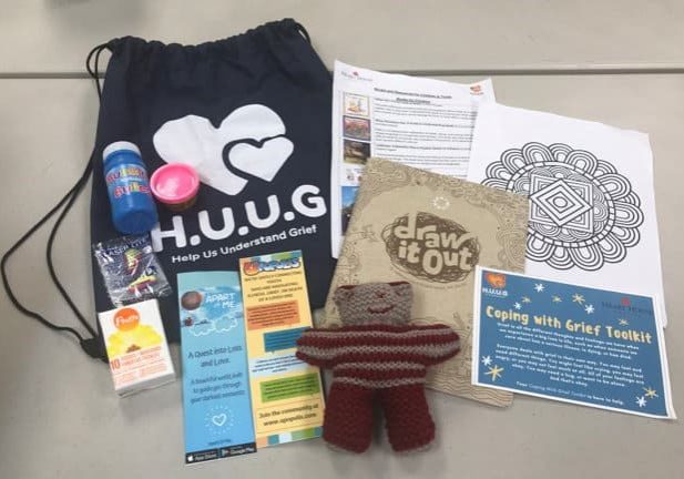 HUUG Grief Kit containing a bag, knit bear, colouring page, bubble solution, pamphlets, and a package of facial tissue.